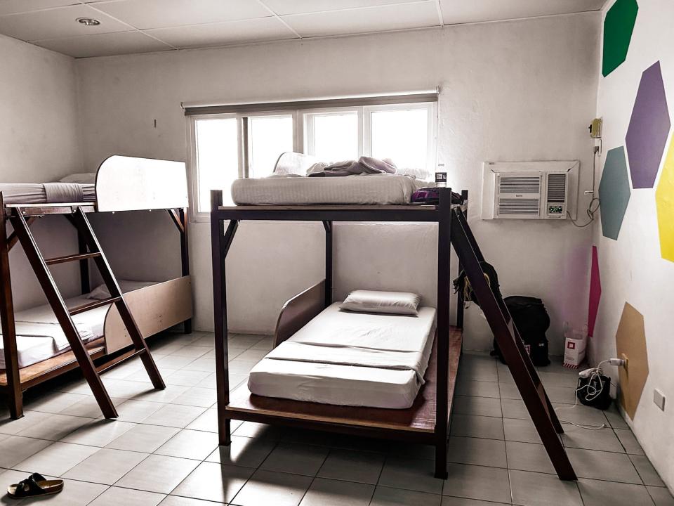 A dormitory room with two sets of bunk beds, an air conditioner, and a wall with a hexagon wallpaper on it.