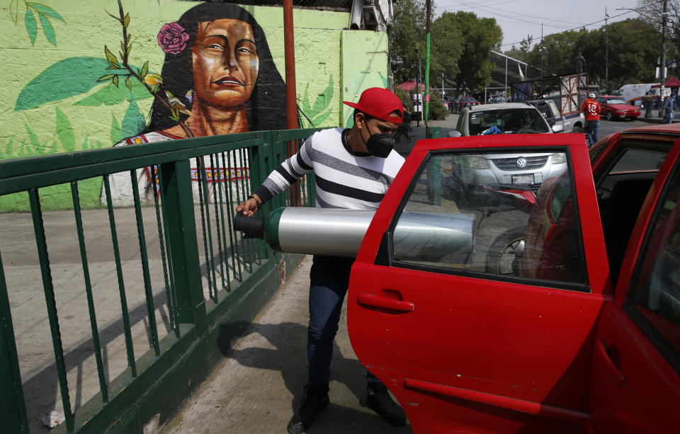A person loads into the back seat of a car a tank filled with oxygen for a family member sick with COVID-19, in the Iztapalapa borough of Mexico City, Friday, Jan. 15, 2021. The city offers free oxygen refills for COVID-19 patients. (AP Photo/Marco Ugarte)