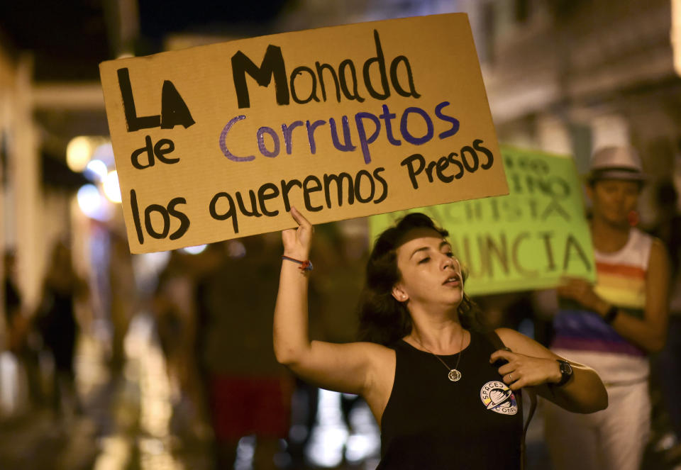 Dozens of citizens protest near the executive mansion denouncing a wave of arrests for corruption that has shaken the country and demanding the resignation of Gov. Ricardo Rosello, in San Juan, Puerto Rico, Thursday, July 11, 2019. Puerto Rico's former secretary of education and 5 other people have been arrested on charges of steering federal money to unqualified, politically connected contractors. U.S. Attorney for Puerto Rico Rosa Emilia Rodríguez said Gov. Rossello was not involved in the investigation. The sign up front reads in Spanish "We want that herd of corrupt officials in prison." (AP Photo/Carlos Giusti)