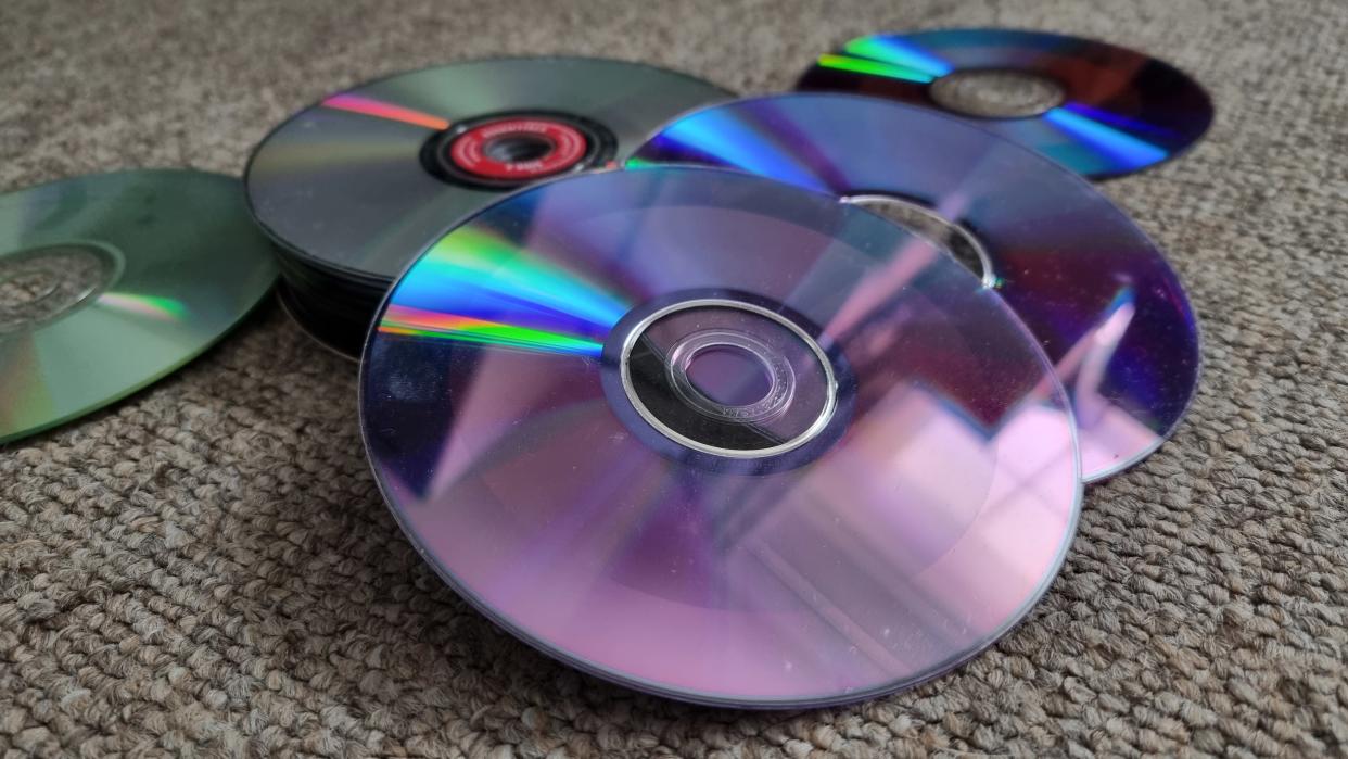  A collection of upturned CDs, DVDs and Blu-rays on a carpeted floor. 