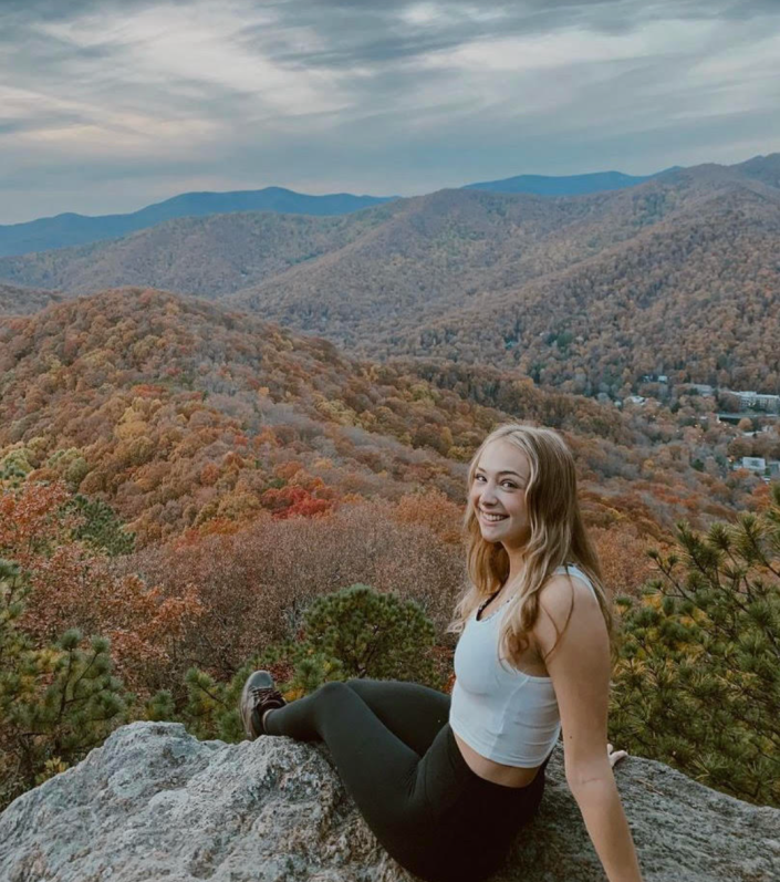 Kelstyn sitting on a rock formation overlooking a wooded area