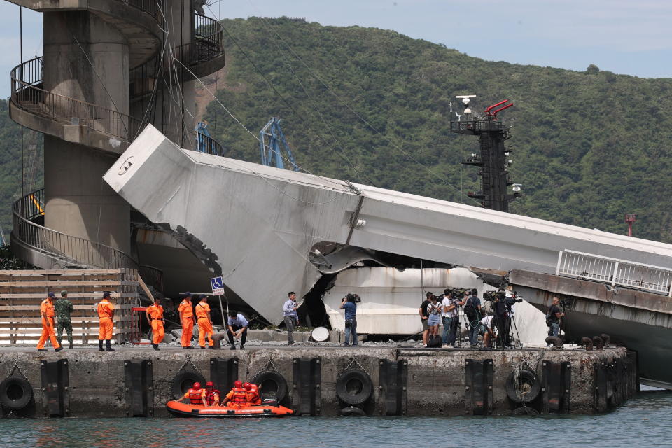 Rescue workers and media can be seen at the cement footing of the bridge hangs in the air.