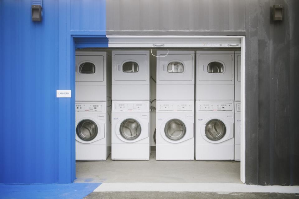 A communal laundry with stacked washers and dryers inside a blue and gray building.