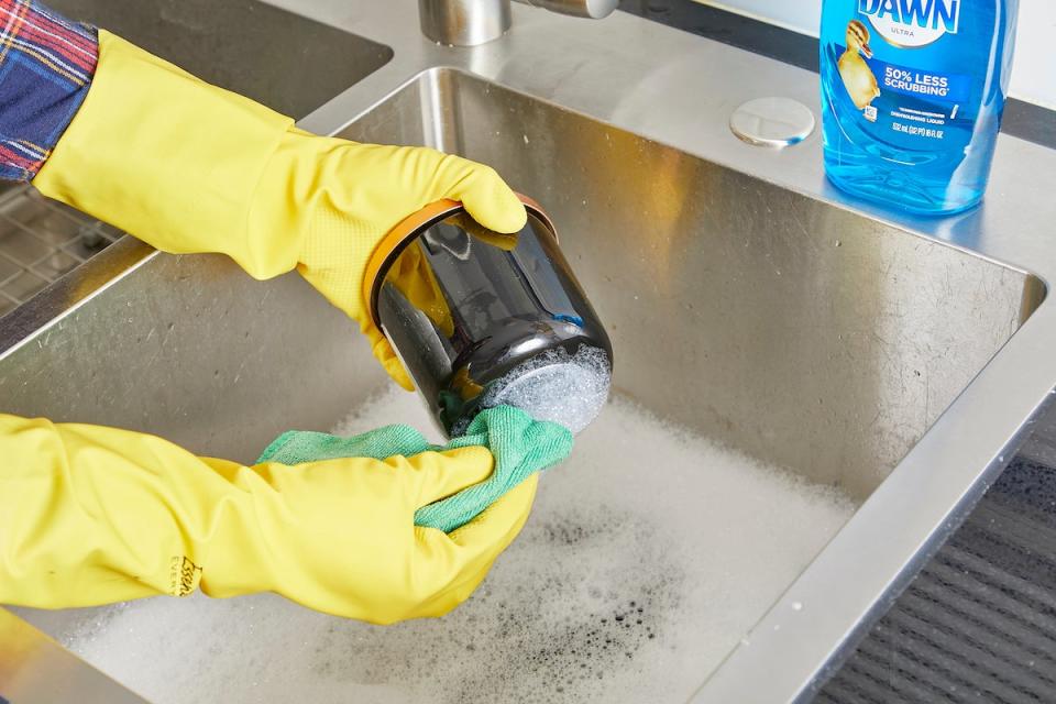 Woman uses dish soap and hot water to remove sticker from jar.