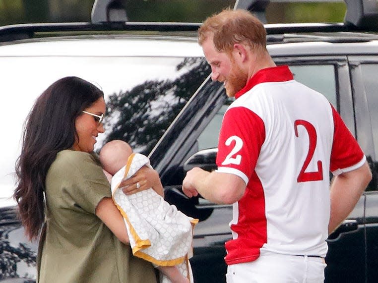 Meghan Markle, holding Archie, talks with Prince Harry while standing outside a black car