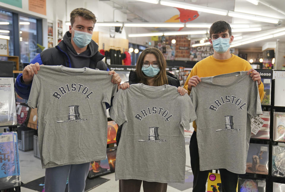 Customers inside Rough Trade in Bristol, England, Saturday Dec. 11, 2021, hold T-shirts designed by street artist Banksy, being sold to support four people facing trial accused of criminal damage in relation to the toppling of a statue of slave trader Edward Colston. The anonymous artist posted on Instagram pictures of limited edition grey souvenir T-shirts which will go on sale on Saturday in Bristol. The shirts have a picture of Colston's empty plinth with a rope hanging off, with debris and a discarded sign nearby. (Jacob King/PA via AP)