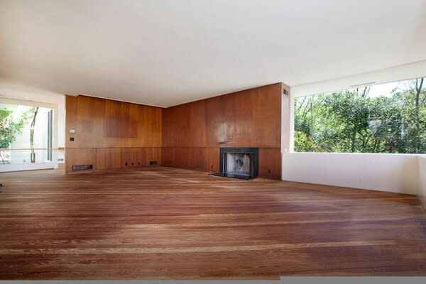 The original living room had worn wood floors and a fireplace near a window.