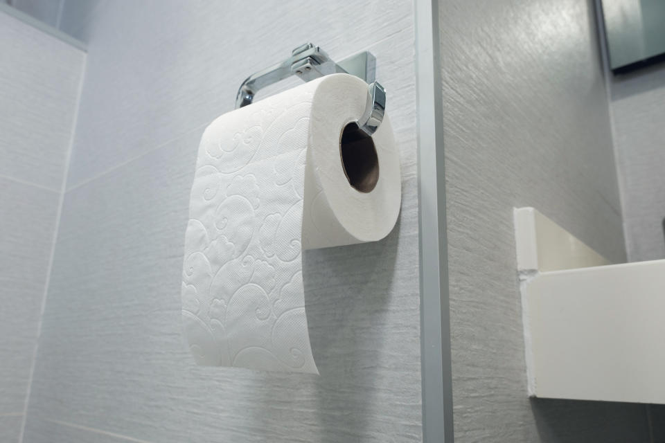 A roll of toilet paper hanging on a holder against a tiled bathroom wall