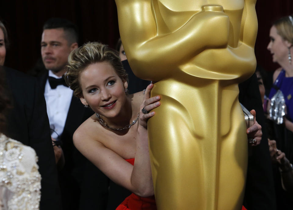 Jennifer Lawrence, best supporting actress nominee for her role in the film "American Hustle", peeks around an Oscar statue on the red carpet as actor Brad Pitt (L) looks on at the 86th Academy Awards in Hollywood, California March 2, 2014. REUTERS/Adrees Latif (UNITED STATES  - Tags: ENTERTAINMENT)(OSCARS-ARRIVALS)