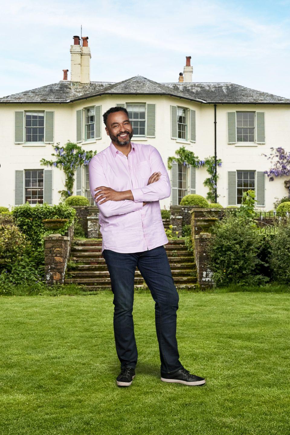 martin from my mum, your dad wearing a pink shirt, standing in front of an estate with his arms folded across his chest