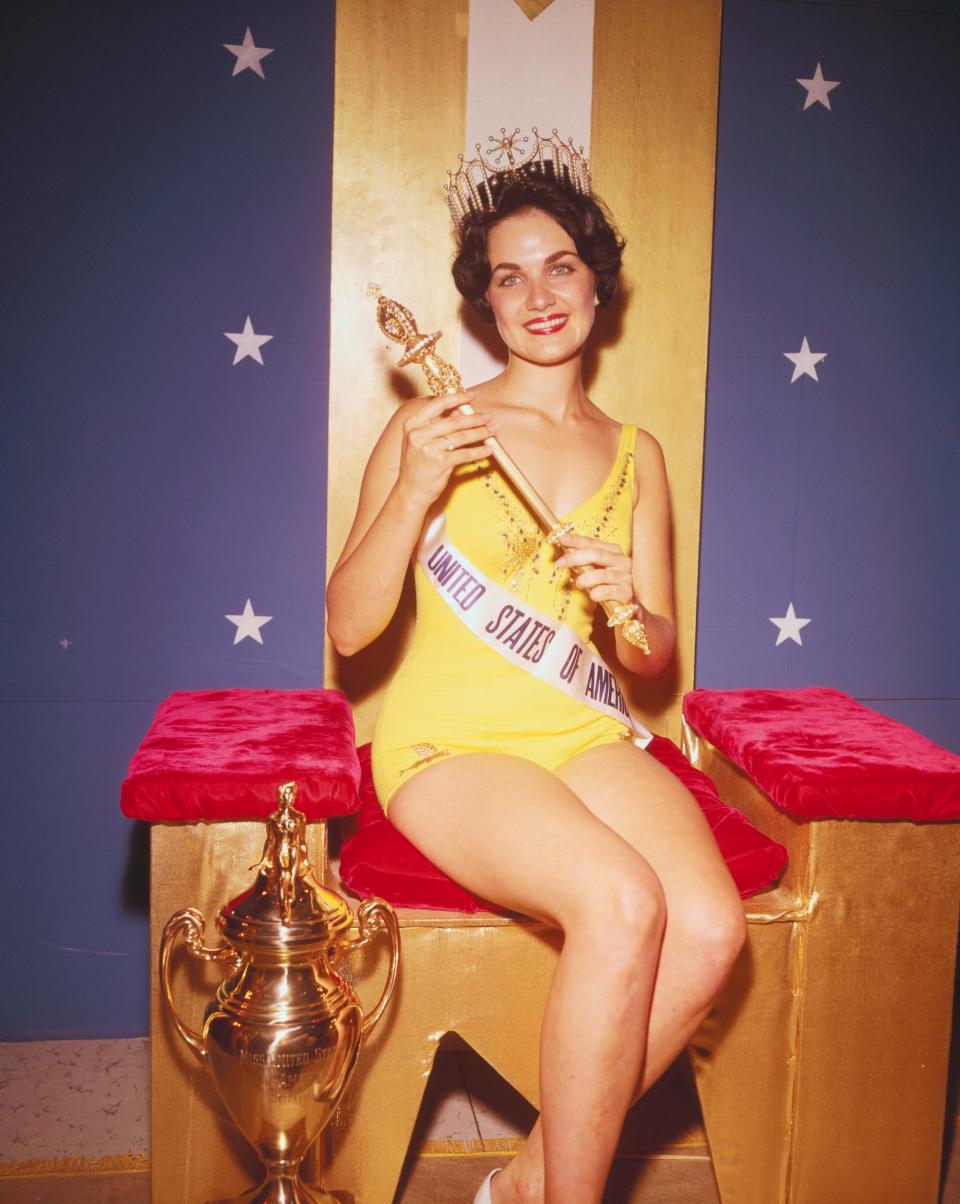 Miss USA 1960 Linda Bement sits on a throne holding a scepter and wearing a tiar.