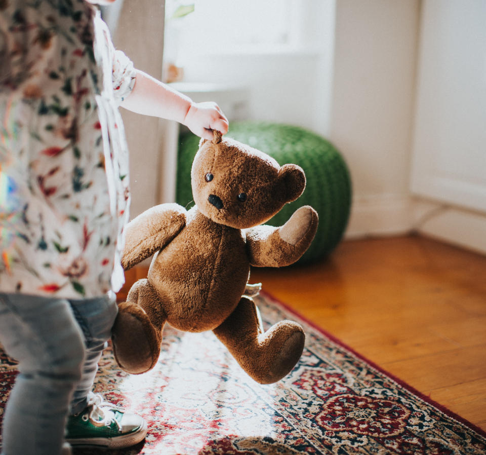 Small child holding a brown teddy bear by the ear