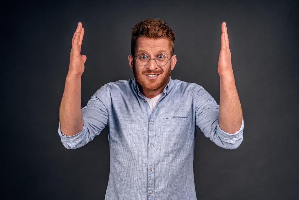 Desperate upset guy looking at his favorite player making huge mistake, feeling disappointed and shocked, standing worred over gray wall with raised hands and nervous expression in glasses and shirt.