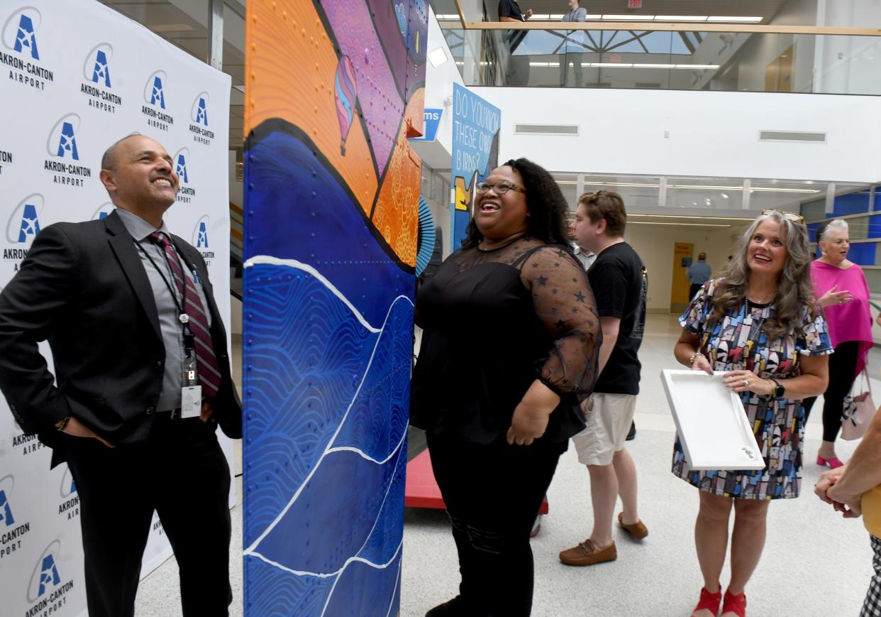 Ren Camacho, president and CEO of the Akron-Canton Airport, looks over the art of Jessica Travis, as fellow artist Tracy Dawn Brewer, right, looks on following the unveiling of Wing Art at the airport on Thursday.