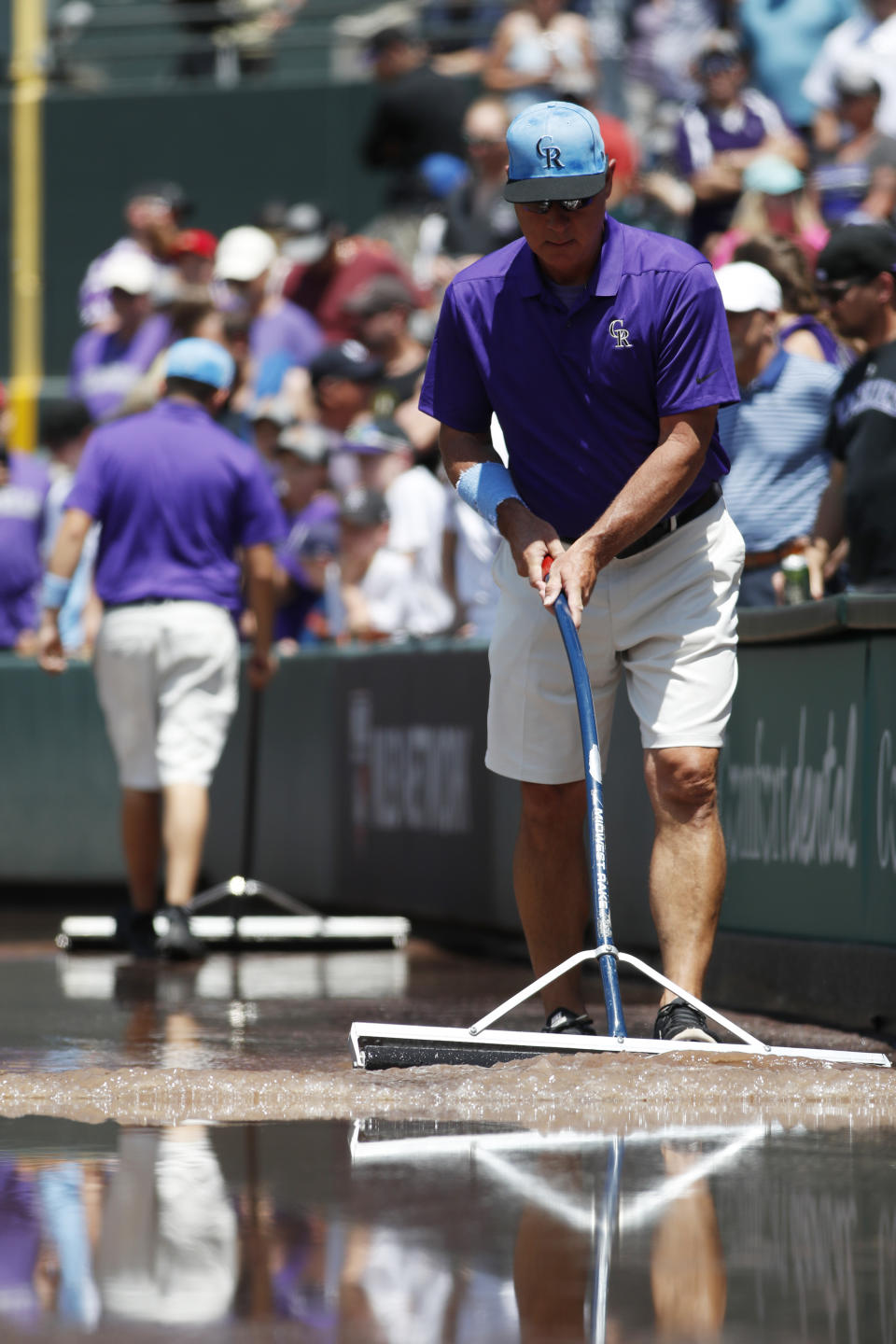 Mark Razum pushes water along the right-field stands after water discharged onto the field to create a lake in the first inning of a baseball game between the San Diego Padres and the Colorado Rockies, Sunday, June 16, 2019, in Denver. (AP Photo/David Zalubowski)