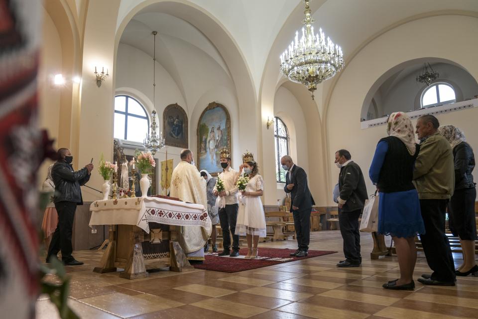 In this photo taken on Sunday, May 24, 2020, Father Vasyl Gasynets, Ukrainian Greek Catholic Church priest, center back to a camera, conducts a religion service during Anatoliy Megeden and Svetlana Megeden wedding ceremony at a church in Chernivtsi, Ukraine. Gasynets has returned to conducting services at his Greek Catholic church in priestly raiment, but wearing a mask while distributing communion. (AP Photo/Evgeniy Maloletka)