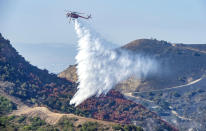 With hand crews on the ground at bottom left, a helicopter drops water onto hot spots from the Silverado Fire off Santiago Canyon Road in Whiting Ranch Wilderness Park on Wednesday, Oct. 28, 2020, near Lake Forest, Calif. (Mark Rightmire/The Orange County Register via AP)