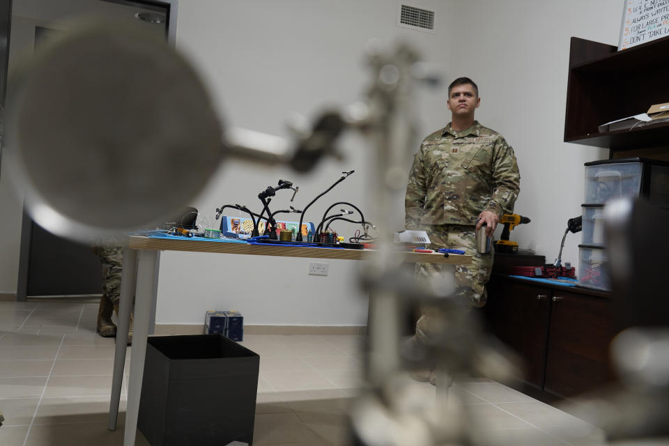 U.S. Air Force Capt. Barrett Kopel stands in a workspace for Task Force 99 while listening to a colleague at Al-Udeid Air Base, Qatar, Friday, Dec. 2, 2022. As over a million World Cup fans fill stadiums with cheers and carry heady optimism through the streets of Doha, some 8,000 American troops are running air wars in Afghanistan, Iraq, Syria and other hotspots in the Middle East mere miles away. (AP Photo/Jon Gambrell)