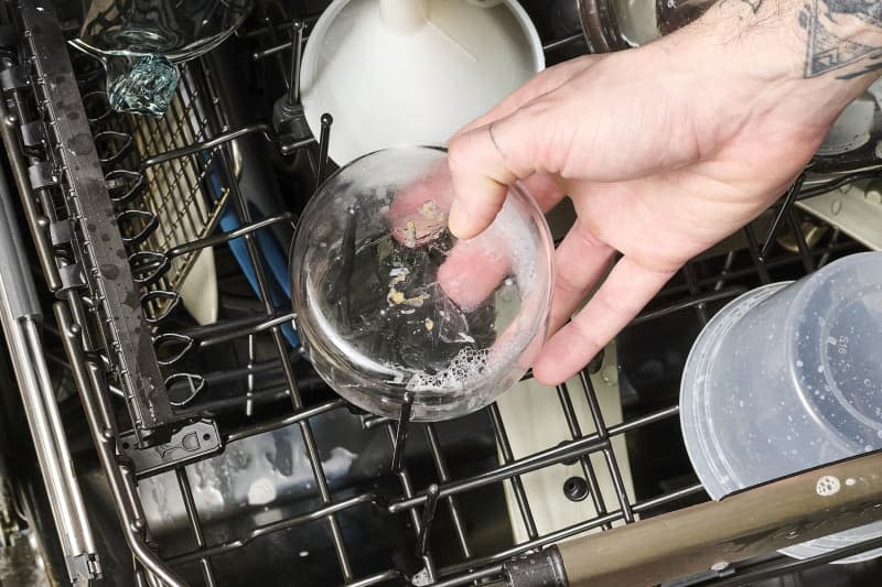 overhead shot of someone putting a cleaned out candle jar into the top rack of the dishwasher.