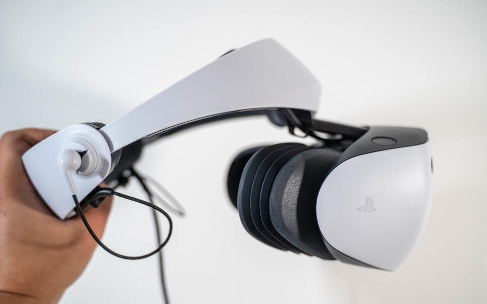 A white PlayStation VR2 headset held up with a hand.