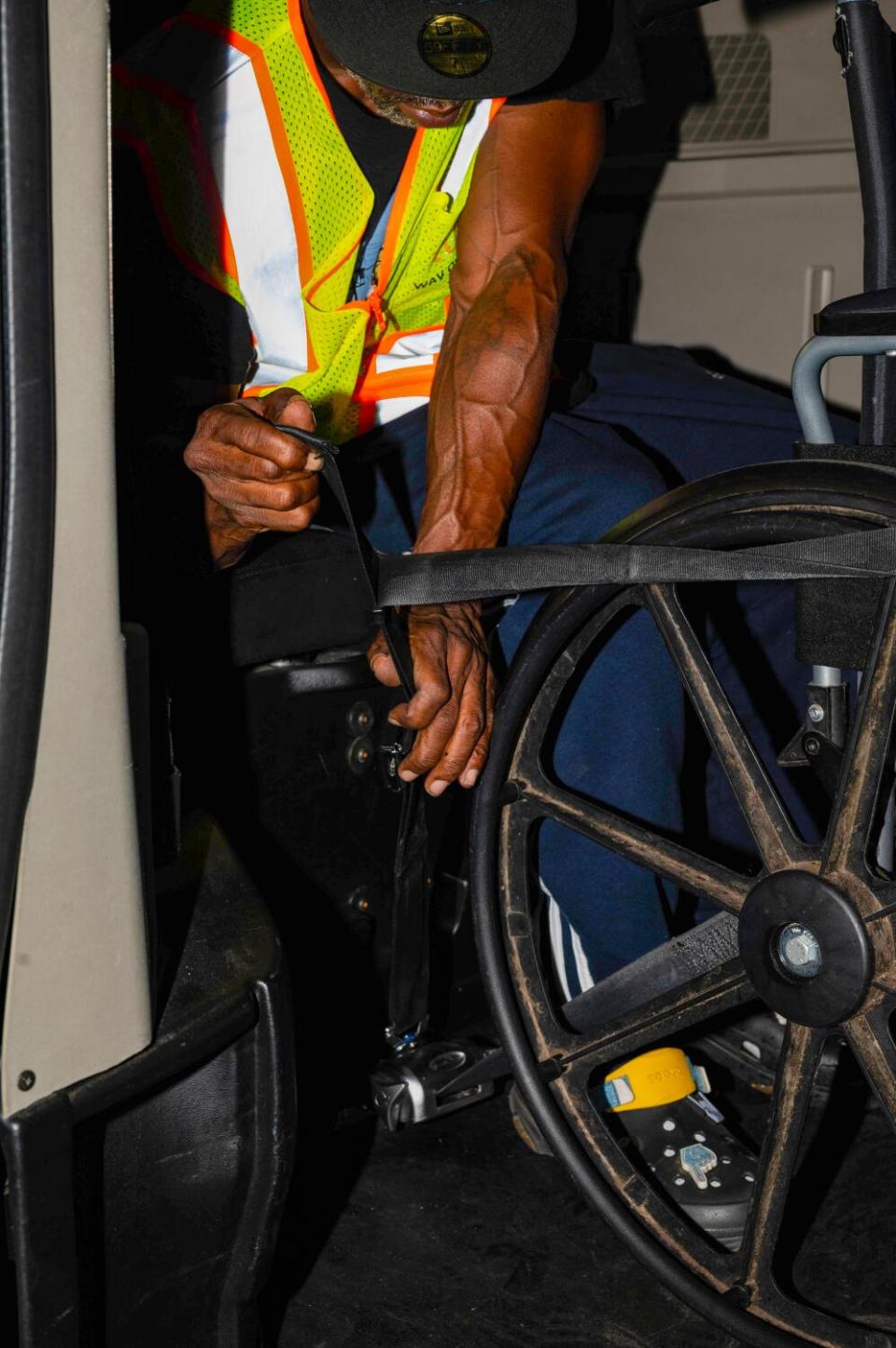 A closeup view of a man in a green vest secures a wheelchair into an accessible Uber.