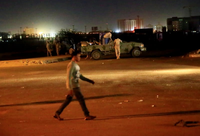 A civilian walks past members of the Sudanese Rapid Support Forces are seen near the area where gunmen opened fire outside buildings used by Sudan's NISS in Khartoum