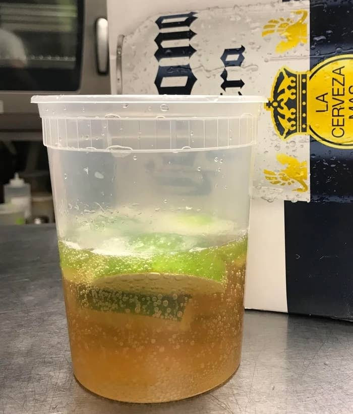 Plastic cup with beverage and lime slices, next to a Corona beer box in a kitchen setting