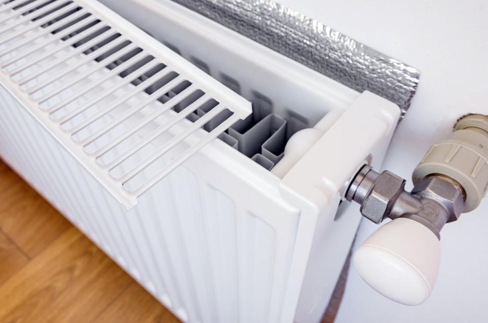 Radiator with grill removed and foil on wall behind it.