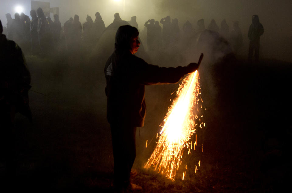 A member of the the Zapatista National Liberation Army, EZLN, lights a firecracker during the 20th anniversary of the Zapatista uprising in the town of Oventic, Chiapas, Mexico, late Tuesday, Dec. 31, 2013. Some commentators warn that Mexico today may look chillingly like it did in 1994. The Zapatista uprising occurred on the very day the North American Free Trade Agreement took effect. The deal, hotly opposed by the left, which opened Mexico’s markets to U.S. goods. This year, Mexico approved another major opening _ energy reforms that will allow private and foreign firms to drill for oil in Mexico _ leaving the left angry and frustrated. (AP Photo/Eduardo Verdugo)