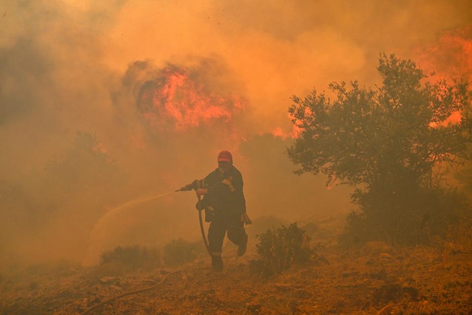 A firefighter runs away from blazes as he tries to control a wildfire in New Peramos, near Athens, on July 19, 2023.