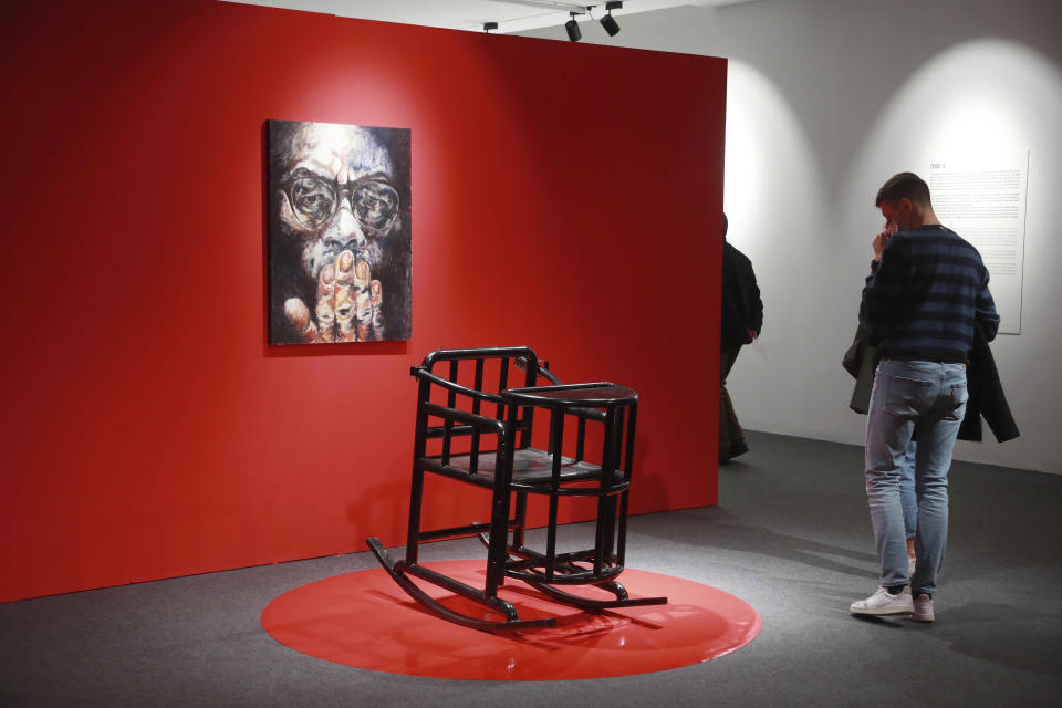 Visitors walk past a torture chair during the opening of artist Badiucao's exhibition in the Santa Giulia Museum, in Brescia, Saturday, Nov. 13, 2021. A provocative exhibit by dissident Chinese artist Badiucao opened Saturday in the industrial northern Italian city of Brescia despite pressure from the Chinese embassy in Rome to cancel it. A letter from the embassy included veiled economic threats, noting Italy’s trade with China, in a bid to prevent the first solo exhibit by Badiucao — the pseudonym used by the artist whose work takes aim at China's policies and human rights record. (AP Photo/Felice Calabro')