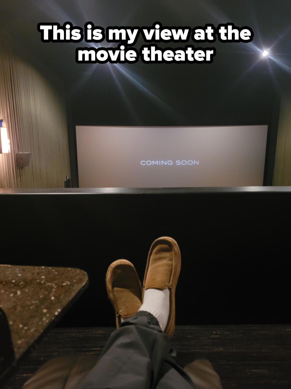 Person in a theater with feet on railing, "COMING SOON" on screen