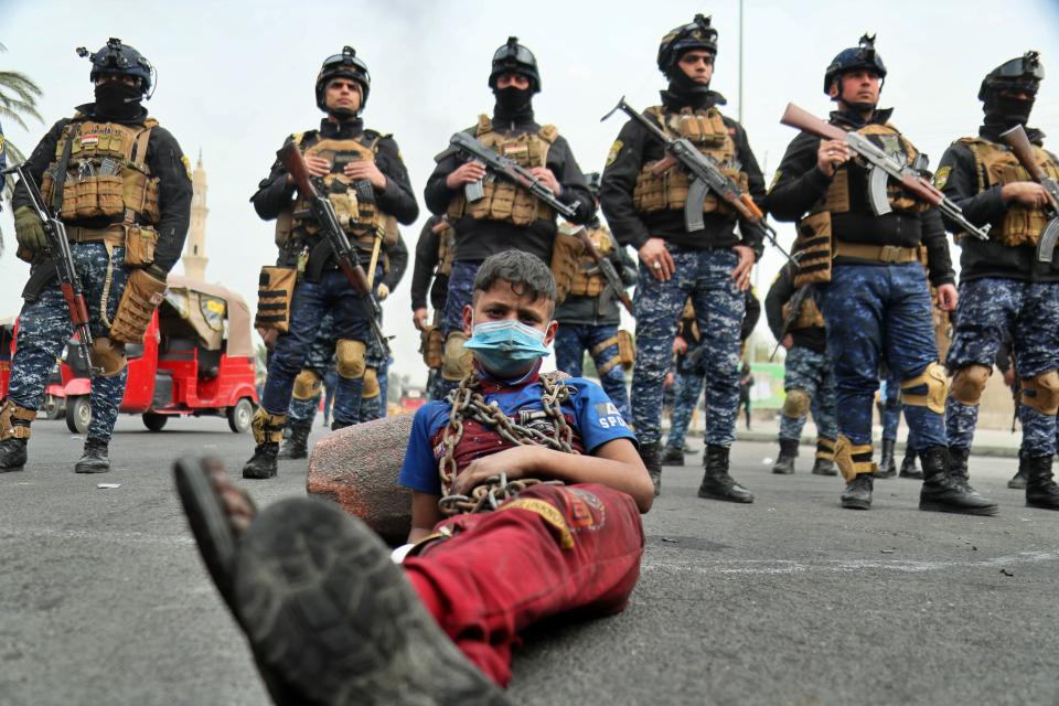 Anti-government protesters stage a sit-in while security forces stand guard during ongoing protests in downtown Baghdad, Iraq, Sunday, Jan. 19, 2020. Black smoke filled the air as protesters burned tires to block main roads in the Iraqi capital Baghdad, expressing their anger at poor services and shortages despite religious and political leaders calling for calm. (AP Photo/Hadi Mizban)