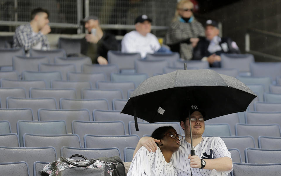 Fans sit in the rain during a rain delay before a baseball game between the New York Yankees and the Baltimore Orioles at Yankee Stadium, Sunday, March 31, 2019, in New York. (AP Photo/Seth Wenig)