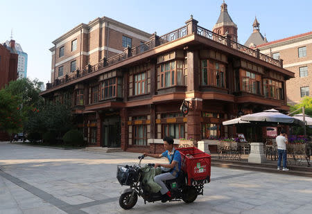 A delivery driver rides past a western style building in central Tianjin, China, May 25, 2018. REUTERS/Yawen Chen