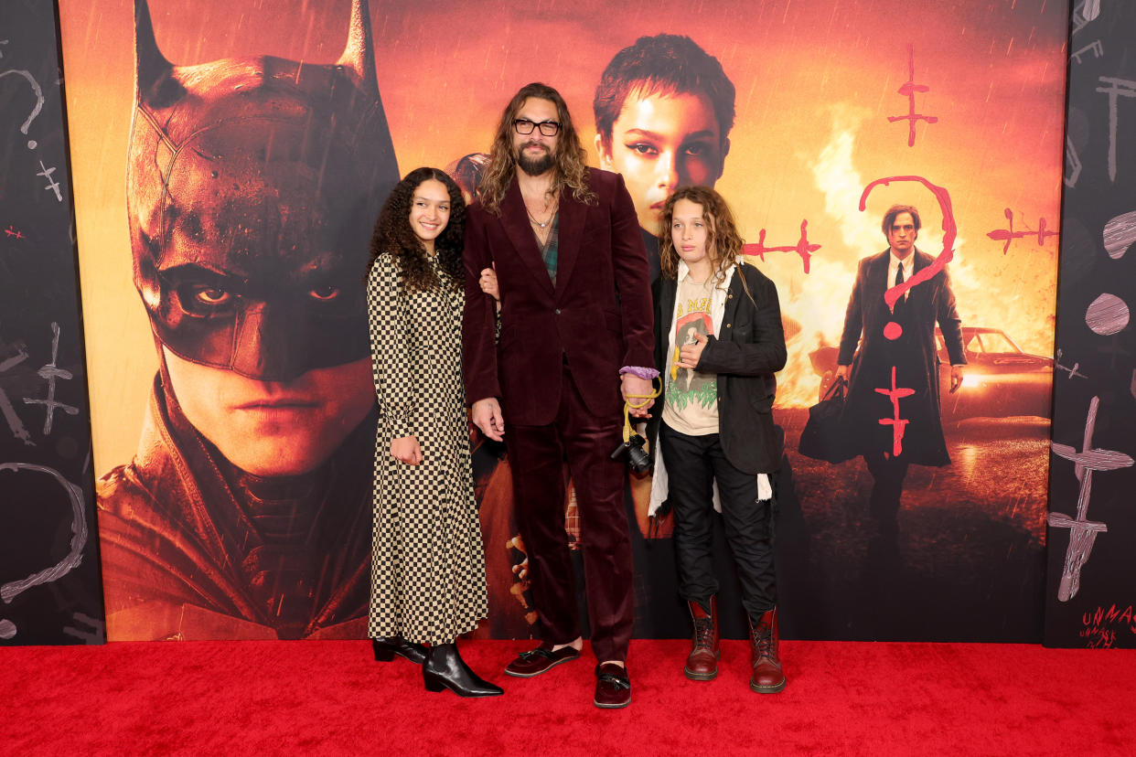 Mamoa in a purple velvet suit with his two young kids standing in front of a batman poster on the red carpet (Cindy Ord / WireImage)