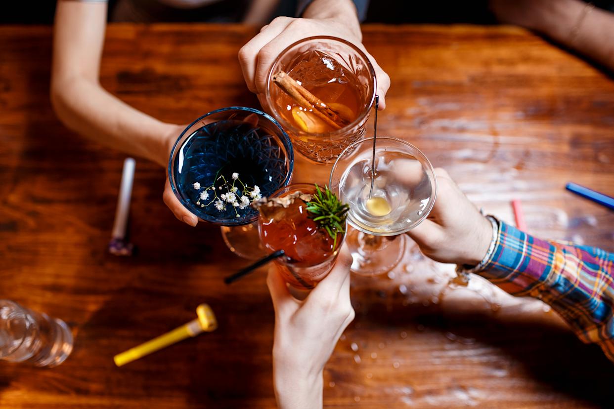 friends clinking by glasses with various alcoholic cocktails at table,close up top view