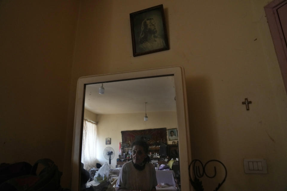 Marie Orfali, 76, is reflected in a mirror under a picture of Jesus in her apartment in Beirut, Lebanon, Tuesday, June 15, 2021. Tiny and bowed by age, Marie Orfali makes the trip five times a week from her Beirut apartment to the local church, a charity and a nearby soup kitchen to fetch a cooked meal for her and her 84-year-old husband, Raymond. (AP Photo/Hassan Ammar)