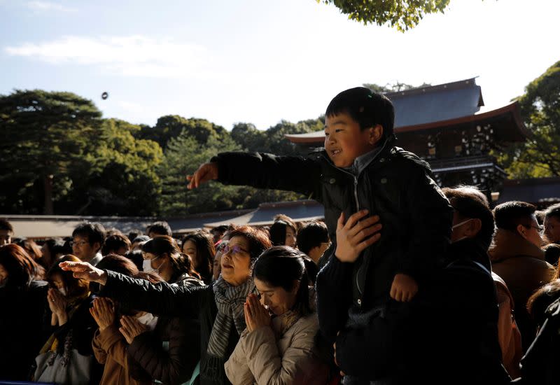 A boy throws a coin as he offers prayers on the first day of the new year at the Meiji Shrine in Tokyo, Japan