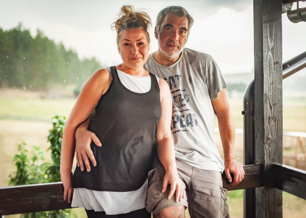 A Gen X couple stand together on the porch of a home