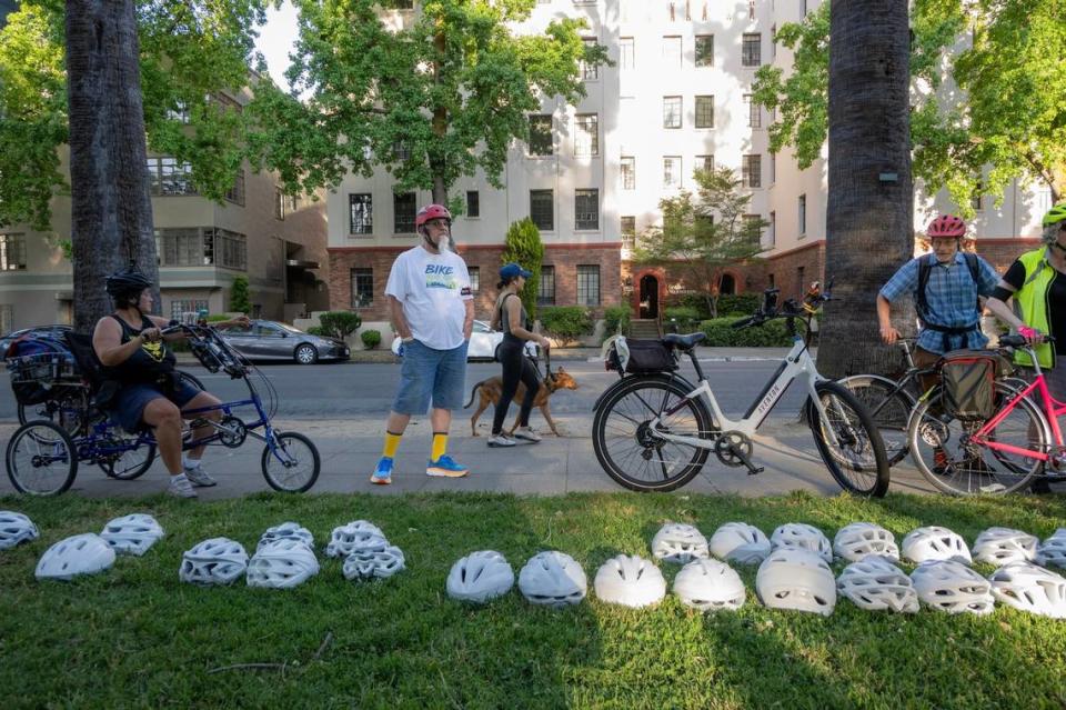 Cole Unger, center, waits on Wednesday at Capitol Park in Sacramento with other cyclists near white helmets signifying those killed while biking before the “Ride of Silence.”