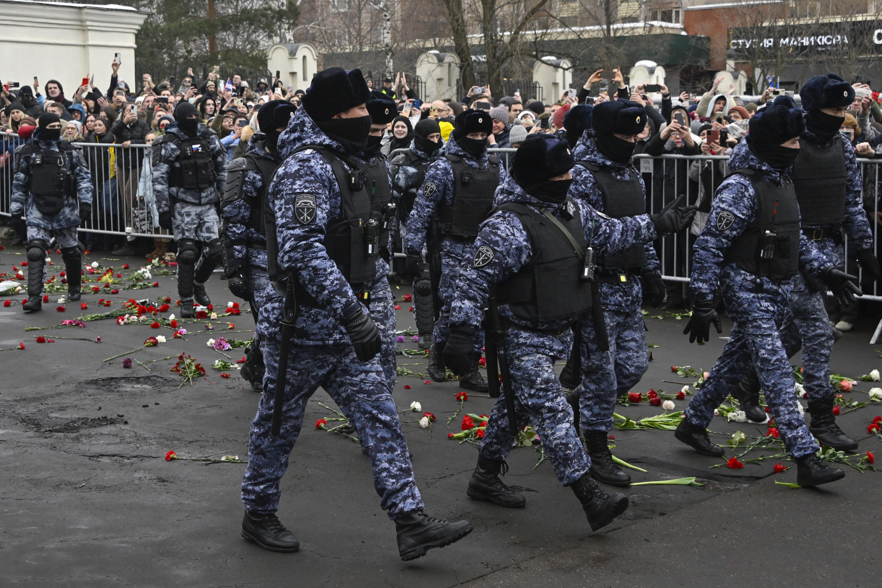 About a dozen police walk outside the church after the funeral service. Throngs of Navalny supporters stand behind barriers in the background.