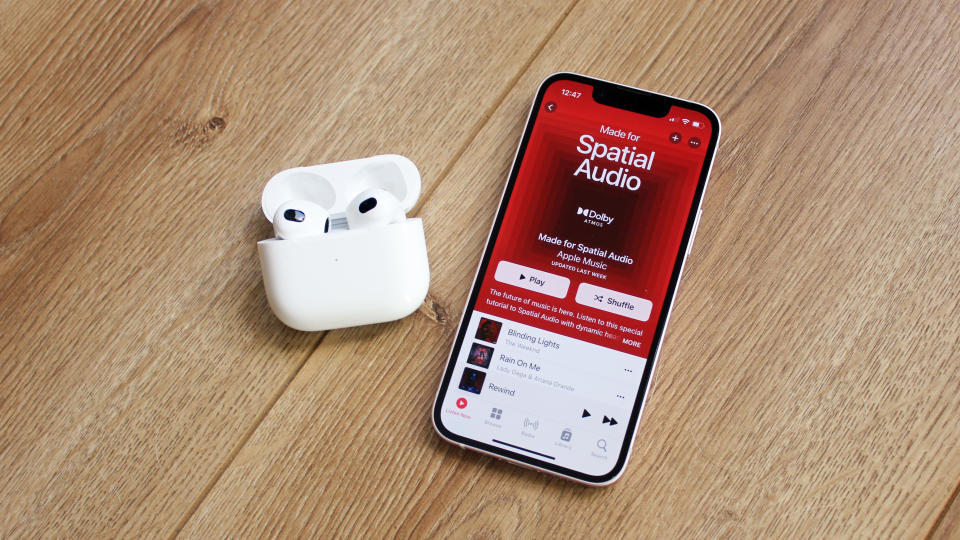The apple airpods 3 true wireless earbuds in their charging case next to an iphone on a wooden surface