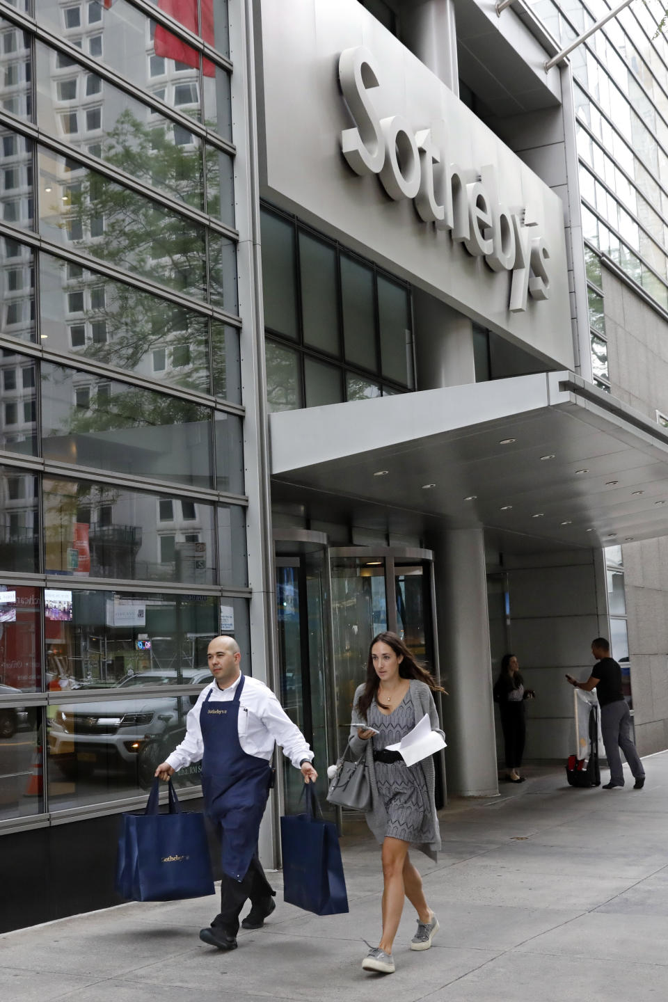 A Sotheby's worker carries bags outside the auction house, in New York, Monday, June 17, 2019. BidFair USA is taking auction house Sotheby's private in a deal valued at $3.7 billion. (AP Photo/Richard Drew)