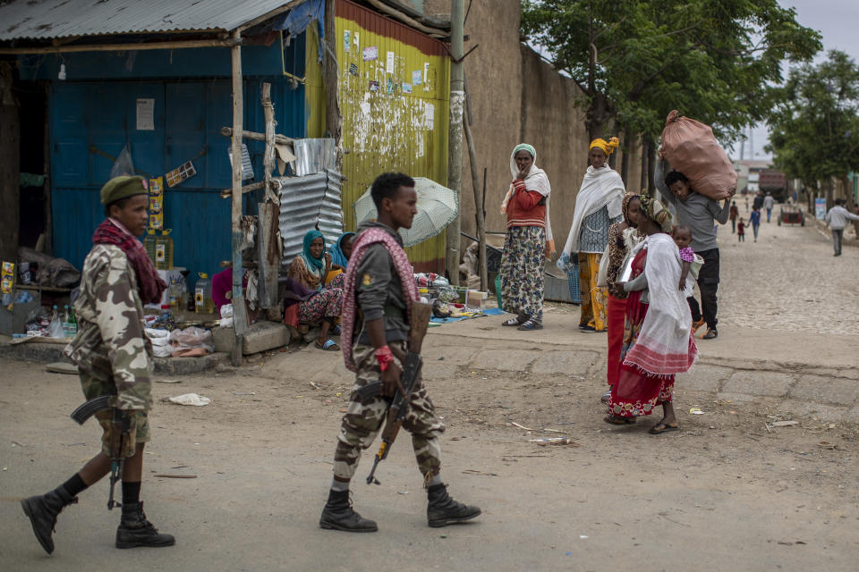 FILE - In this Friday, May 7, 2021 file photo, fighters loyal to the Tigray People's Liberation Front (TPLF) walk past women selling foodstuffs on the street in the town of Hawzen, then-controlled by the group but later re-taken by government forces, in the Tigray region of northern Ethiopia. The Tigray forces that in late June 2021 have retaken key areas after fierce fighting have rejected the cease-fire and vowed to chase out Ethiopian government forces and those of neighboring Eritrea. (AP Photo/Ben Curtis, File)