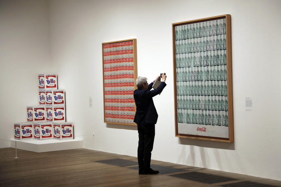 Un hombre toma una foto de la obra de Andy Warhol de 1962 "Green Coca-Cola Bottles" durante una presentación a la prensa de la exposición "Andy Warhol" en el museo Tate Modern de Londres, el martes 10 de marzo del 2020. La muestra estará abierta al público desde el 12 de marzo hasta el 6 de septiembre. (AP Foto/Matt Dunham)