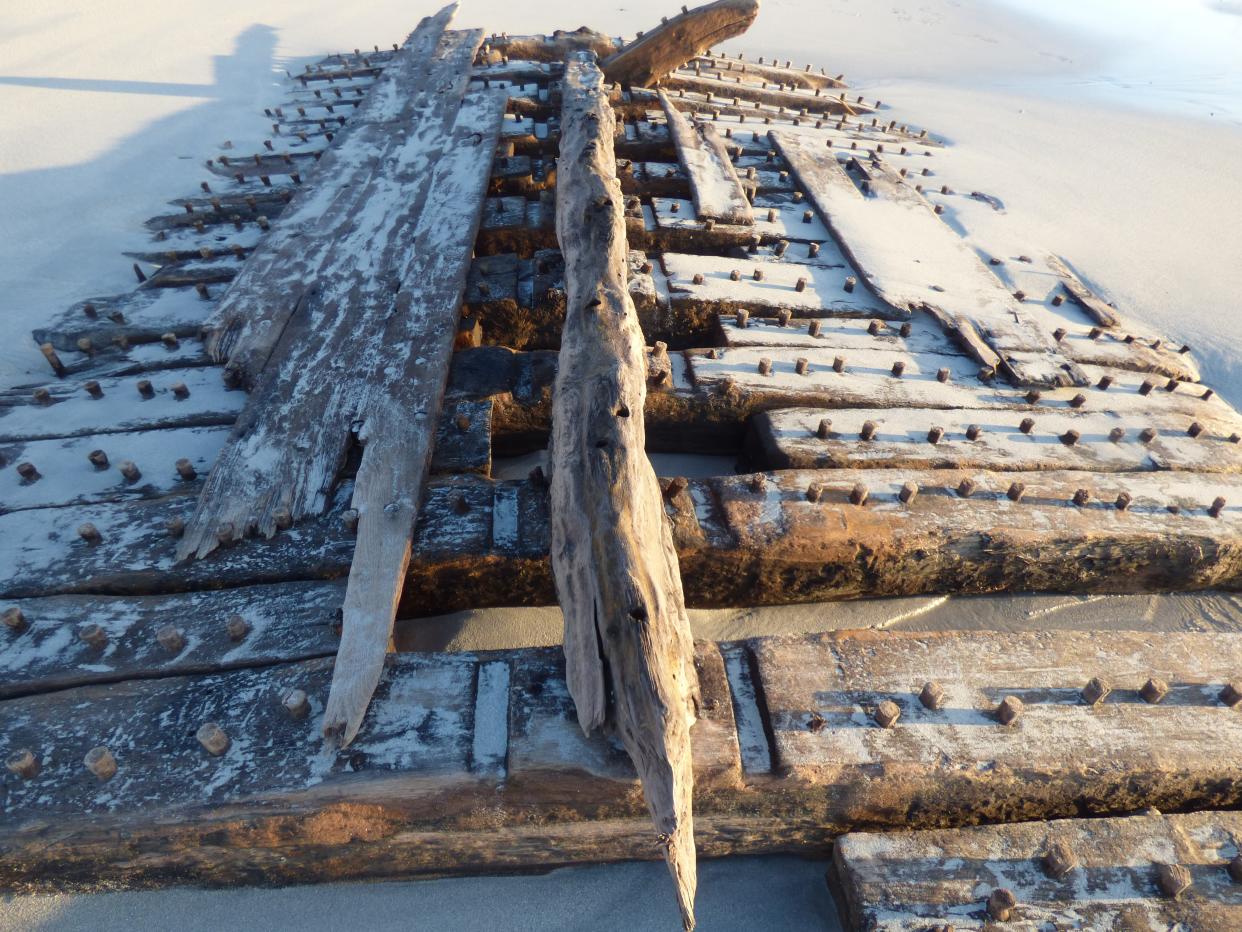 Timbers forming part of a ship, partly covered in sand