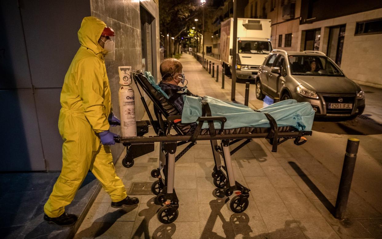 A paramedic wearing full personal protective equipment (PPE) wheels a patient showing coronavirus symptoms from his home to a waiting ambulance - Angel Garcia 