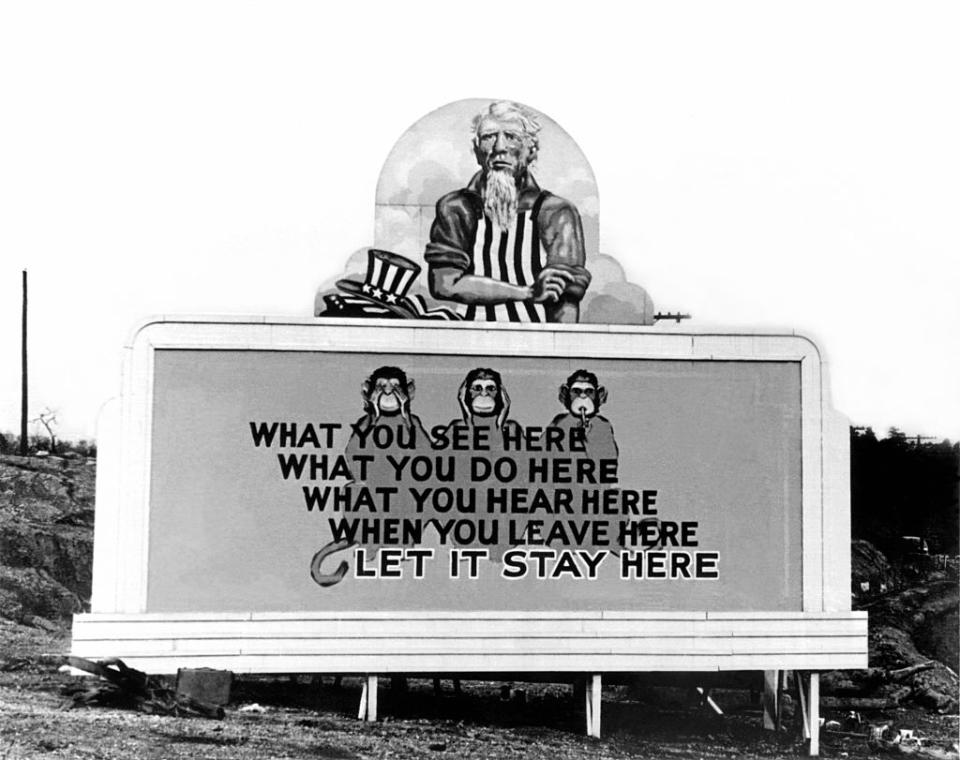 A billboard with an Uncle Sam–type figure above three monkeys (each covering their eyes, ears, or mouth) with the words, "What you see here what you do here what you hear here when you leave here let it stay here"