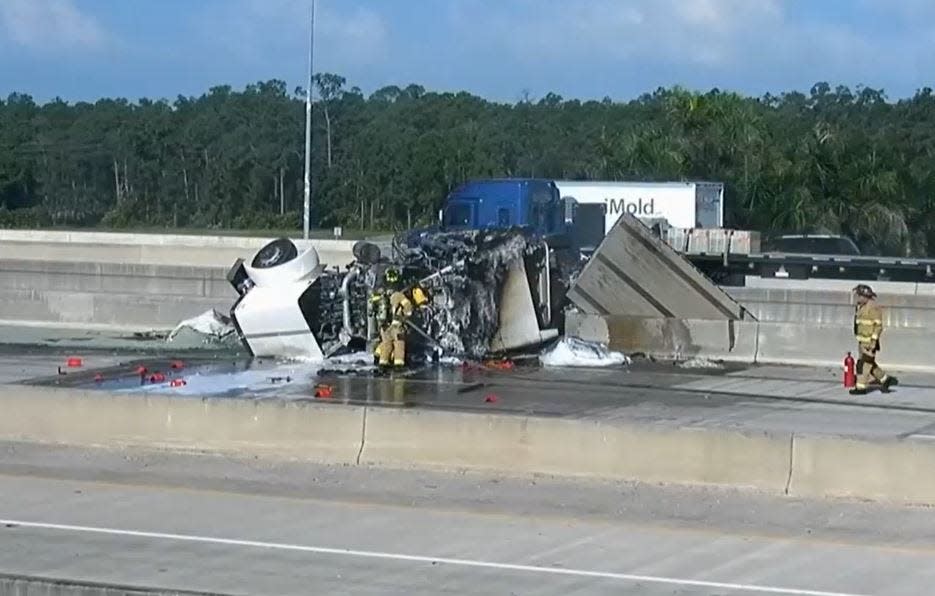 Firefighters spray a fire in a semi tractor trailer truck on Interstate 75 near Alico Road early Friday, the truck's load hanging from the overpass.